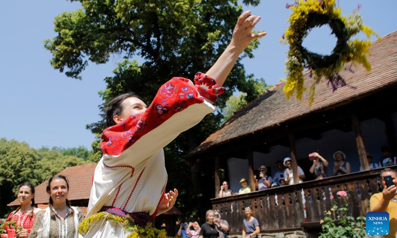 A young girl dressed as a fairy throws her wreath on the roof of a house to see if she will get married this year during the traditional folk festival Sanziene in Bucharest, capital of Romania, June 24, 2023. Ancient traditions mention Sanzienele as gentle fairies that come around summer solstice to bring good luck and good harvest. (Photo by Cristian Cristel/Xinhua)