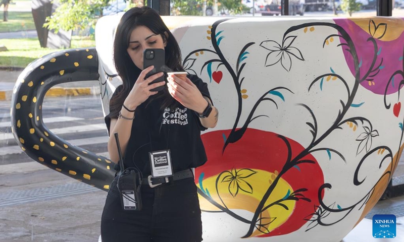 A staff member poses for a photo in front of a coffee artwork during the Sao Paulo Coffee Festival in Sao Paulo, Brazil, on June 23, 2023. (Xinhua/Wang Tiancong)