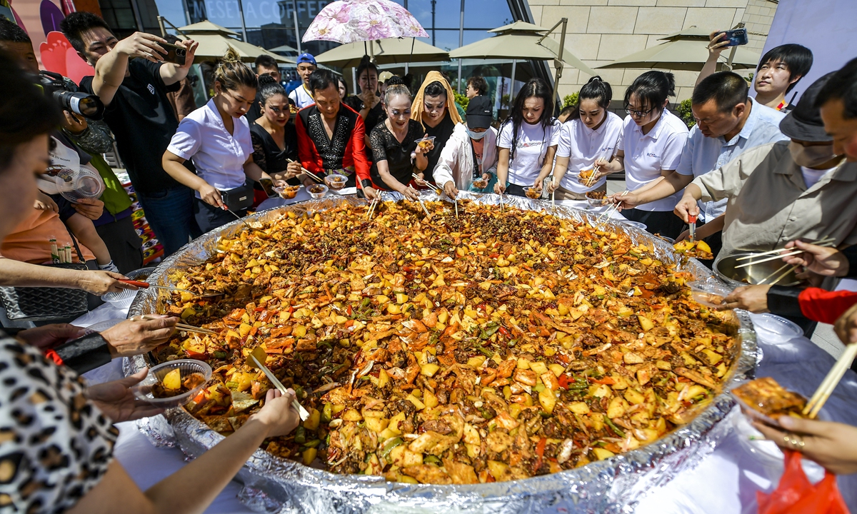 People try dapanji (Lit: big plate chicken) from a huge plate about 5 meters in diameter in Urumqi, Northwest China's Xinjiang Uygur Autonomous Region, on June 28, 2023. A popular dish that originated in Xinjiang, dapanji is mainly stewed with chicken, potatoes and various spices. It is usually served with Xinjiang belt noodles. Photo: VCG