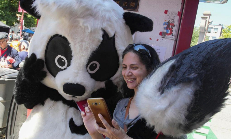 A visitor takes photos with a panda mascot during the 21st Chinatown Festival in Vancouver, British Columbia, Canada, on July 15, 2023. The two-day community family event kicked off on Saturday here. (Photo by Liang Sen/Xinhua)