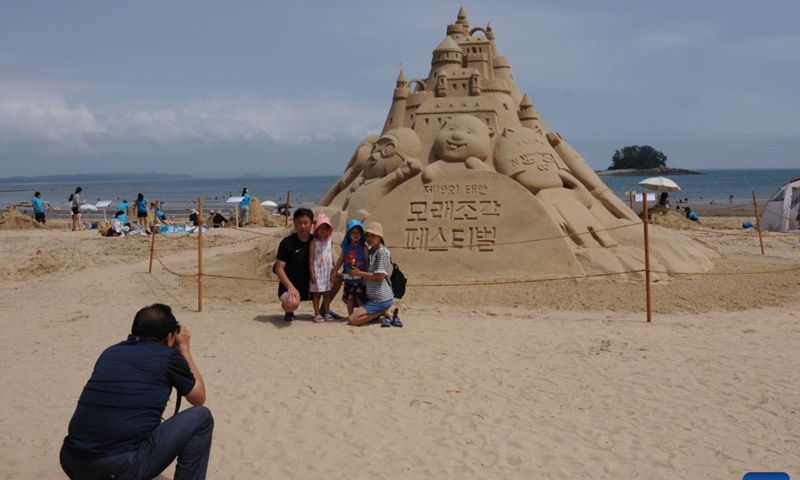 Tourists pose for pictures in front of a sand sculpture during a sand sculpture festival on Yeonpo Beach in Taean County, South Chungcheong Province, South Korea, July 8, 2023. (Xinhua/Zhou Siyu)