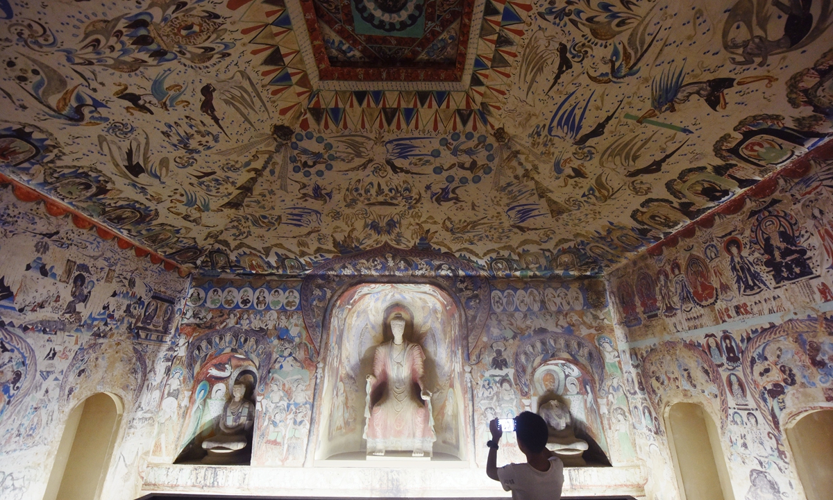 A visitor takes a photo inside a 1:1 replica of the Dunhuang Mogao Grottoes at a Dunhuang cultural relic exhibition held in Hangzhou, East China's Zhejiang Province on July 18, 2023. Grotto No.285, one of the earliest grottoes to be dated by experts, was created in the fourth year of Emperor Wen's reign during the Western Wei Dynasty (535-556). Photo: VCG