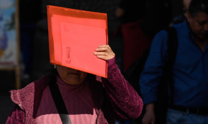 A woman shields her face from the sun while walking in a street during winter time in Santiago, Chile, Aug. 4, 2023. (Photo by Jorge Villegas/Xinhua)
