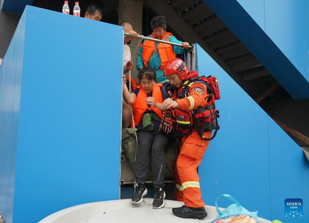 A firefighter helps people to board a rescue boat in Fangshan District of Beijing, capital of China, Aug. 2, 2023. Some parts of the Fangshan District suffered from flood and geological disasters caused by recent rainstorms in the capital city. A rescue team comprised of firefighters, medical workers and volunteers set out to evacuate people afflicted by rainstorms and floods in Pinggezhuang Village of Liulihe Town on Wednesday. (Photo: Xinhua)