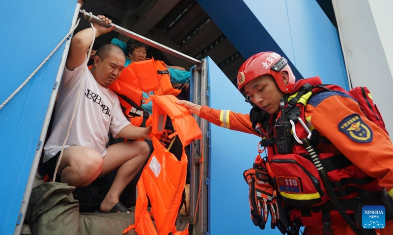 A firefighter distributes life vests to people in Fangshan District of Beijing, capital of China, Aug. 2, 2023. Some parts of the Fangshan District suffered from flood and geological disasters caused by recent rainstorms in the capital city. A rescue team comprised of firefighters, medical workers and volunteers set out to evacuate people afflicted by rainstorms and floods in Pinggezhuang Village of Liulihe Town on Wednesday. (Photo: Xinhua)