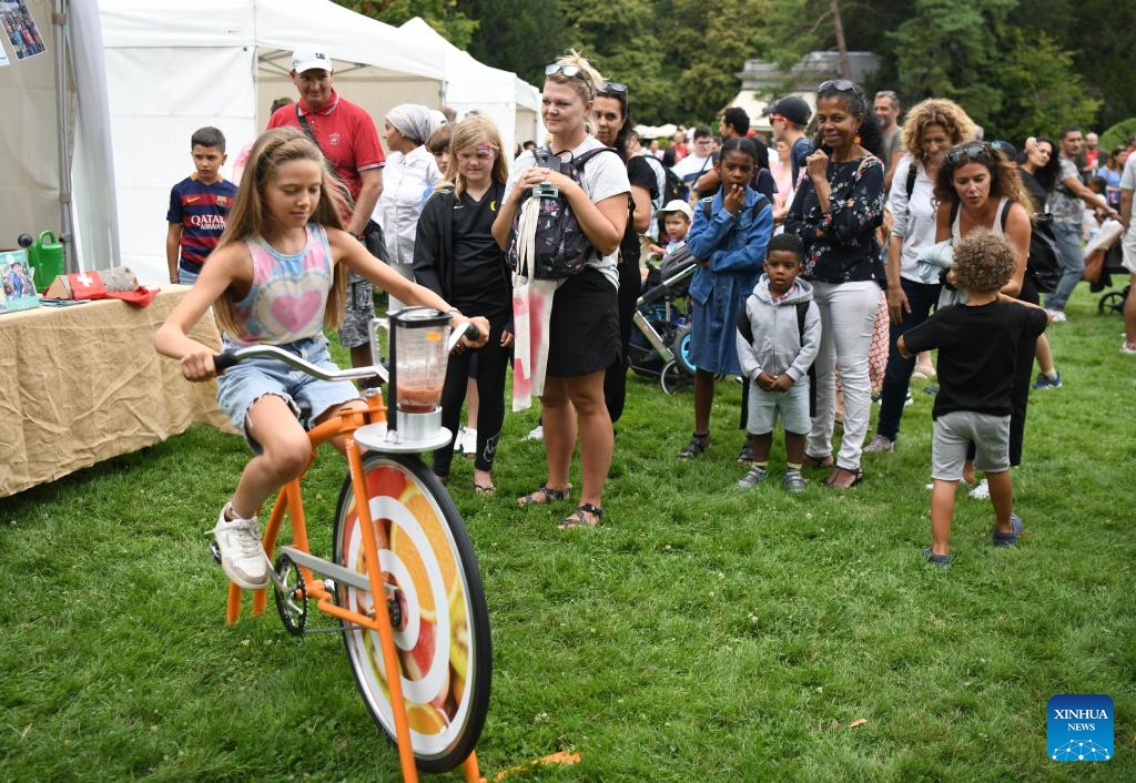 A child tries an environmentally friendly juicer powered by pedaling during an event in commemoration of the Swiss National Day at La Grange Park in Geneva, Switzerland, Aug. 1, 2023.(Photo: Xinhua)