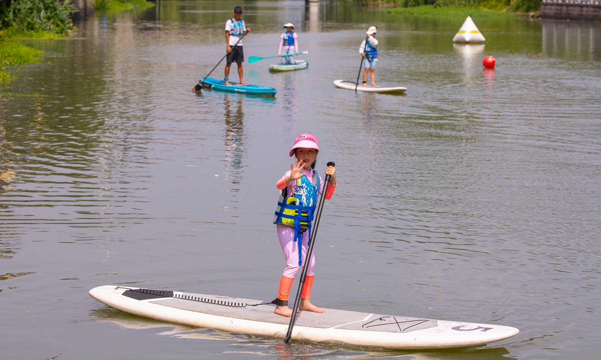 Children and other Hangzhou residents go paddleboarding on a river under the guidance of a professional coach on August 22, 2023. With the 19th Asian Games Hangzhou approaching, a number of rivers in the city are providing free water sports experiences. Photo: VCG