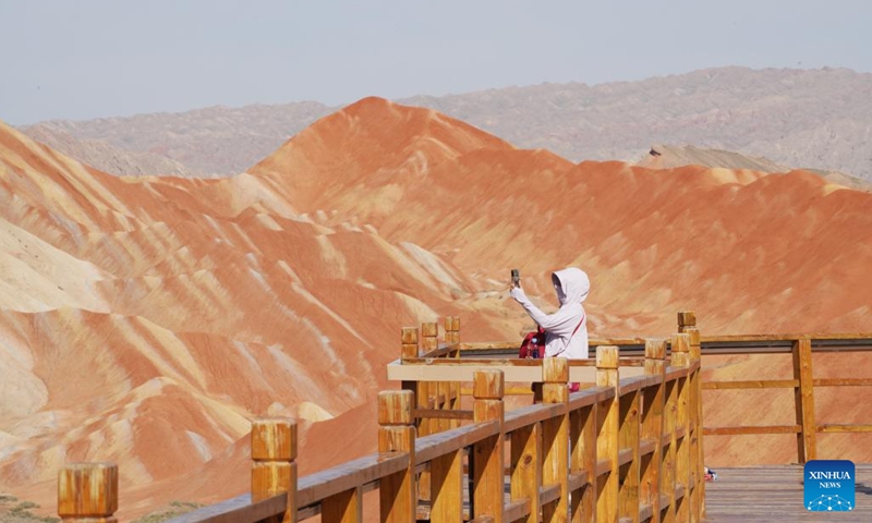 A tourist visits the Danxia National Geological Park in Zhangye, northwest China's Gansu Province, Aug. 7, 2023. Boasting a unique type of geomorphology formed from red-colored sandstones and characterized by steep cliffs, the Danxia National Geological Park has attracted an average of over 35,000 visitors daily since August.(Photo: Xinhua)