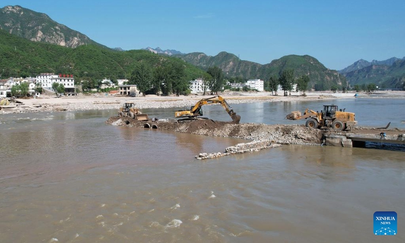 This aerial photo shows workers operating machinery to repair a bridge to Shangzhuang Village, Sanpo Town, Laishui County, in north China's Hebei Province, Aug. 8, 2023. Affected by Typhoon Doksuri, Laishui County suffered heavy rainfall recently and some villages encountered traffic and communication disruptions. At present, the local authorities are mending infrastructure damaged by flood to bring life back to normal as soon as possible.(Photo: Xinhua)