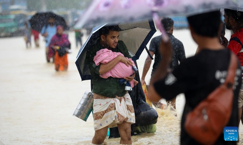 A man holding a baby wades through a flooded road in Chattogram, Bangladesh, on Aug. 9, 2023. Bangladeshi soldiers were deployed on Tuesday to the country's Chattogram region, some 240 km southeast of the capital Dhaka, to tackle its worsening situation of torrential rains. Three incidents of landslides claimed at least six lives in Chattogram's Cox's Bazar district on Monday, which is now home to nearly 1 million Rohingya refugees who are living on the slopes of the hills.(Photo: Xinhua)