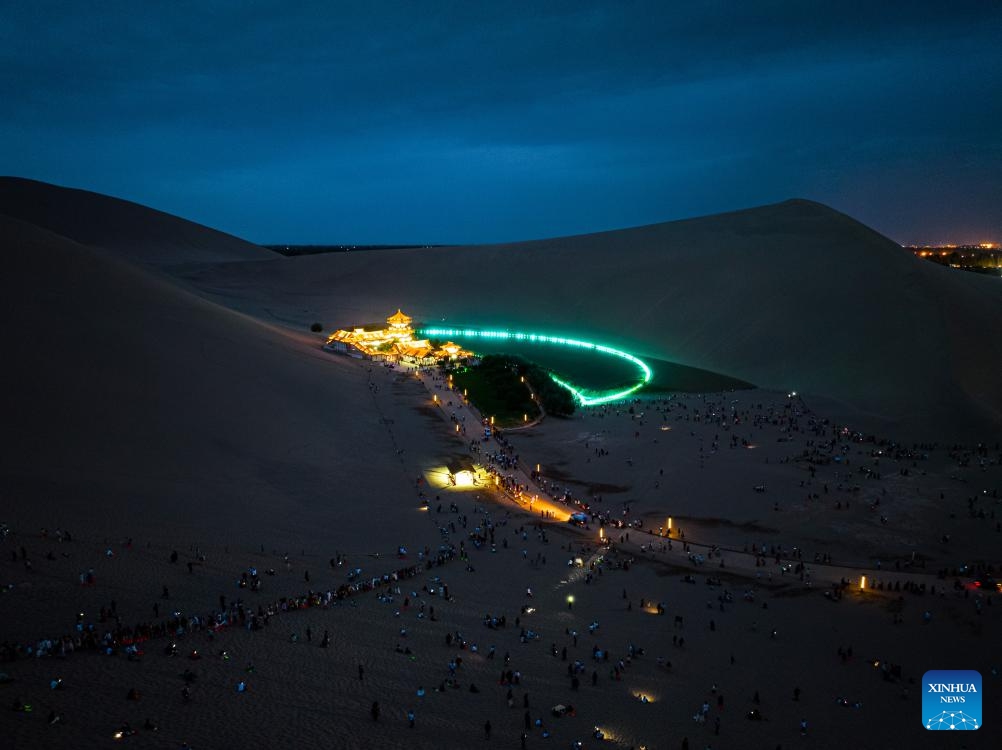 This aerial photo taken on Aug. 8, 2023 shows tourists visiting the Mingsha Mountain and Crescent Spring scenic spot in Dunhuang, northwest China's Gansu Province. The Mingsha Mountain and Crescent Spring scenic spot in Dunhuang has entered its peak tourist season during the summer vacation.(Photo: Xinhua)