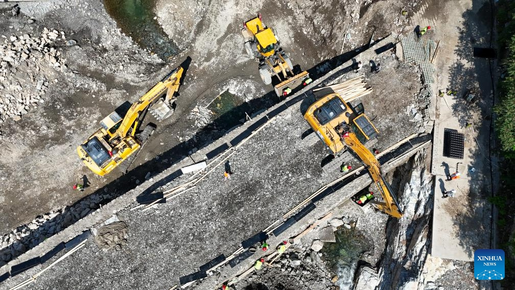 This aerial photo taken on Aug. 23, 2023 shows construction workers rebuilding a bridge in front of the Xiayunling central primary school in Fangshan District of Beijing, capital of China. Due to the influence of heavy rainfall, Xiayunling central primary school in Fangshan District of Beijing had part of its buildings and playground collapsed, and the road and bridge in front of the school damaged.(Photo: Xinhua)