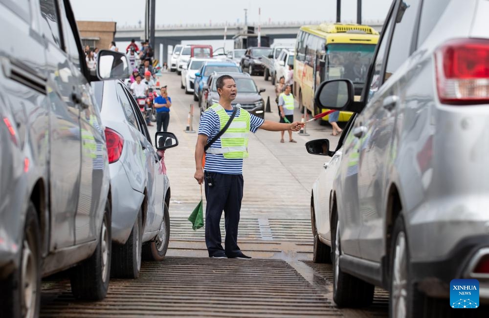 This photo taken on July 1, 2023 shows Zhong Helin, a sailor of the cross-river vehicle ferry linking Nixi Town and Juexi Town in Xuzhou District of Yibin in southwest China's Sichuan Province, directing vehicles on the deck. The cross-river vehicle ferry service that links Nixi Town and Juexi Town in Xuzhou District of Yibin started in May of 1992.(Photo: Xinhua)