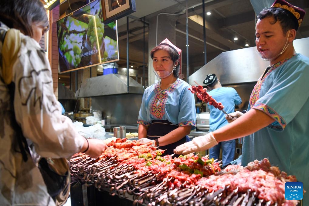 Customers select barbecue at the Xinjiang International grand bazaar in Urumqi, northwest China's Xinjiang Uygur Autonomous Region, Aug. 16, 2023. Xinjiang International Grand Bazaar, inaugurated in 2003, now serves as a key sightseeing and shopping destination, mainly selling local specialties such as dried fruits, medicinal herbs, carpets, jades, ethnic costumes and musical instruments.(Photo: Xinhua)