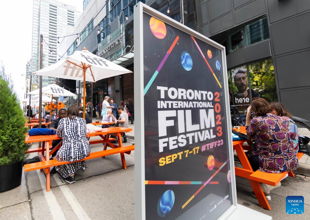 People sit near a Toronto International Film Festival (TIFF) poster in Toronto, Canada, on Sept. 7, 2023. The TIFF kicked off here on Thursday.(Photo: Xinhua)