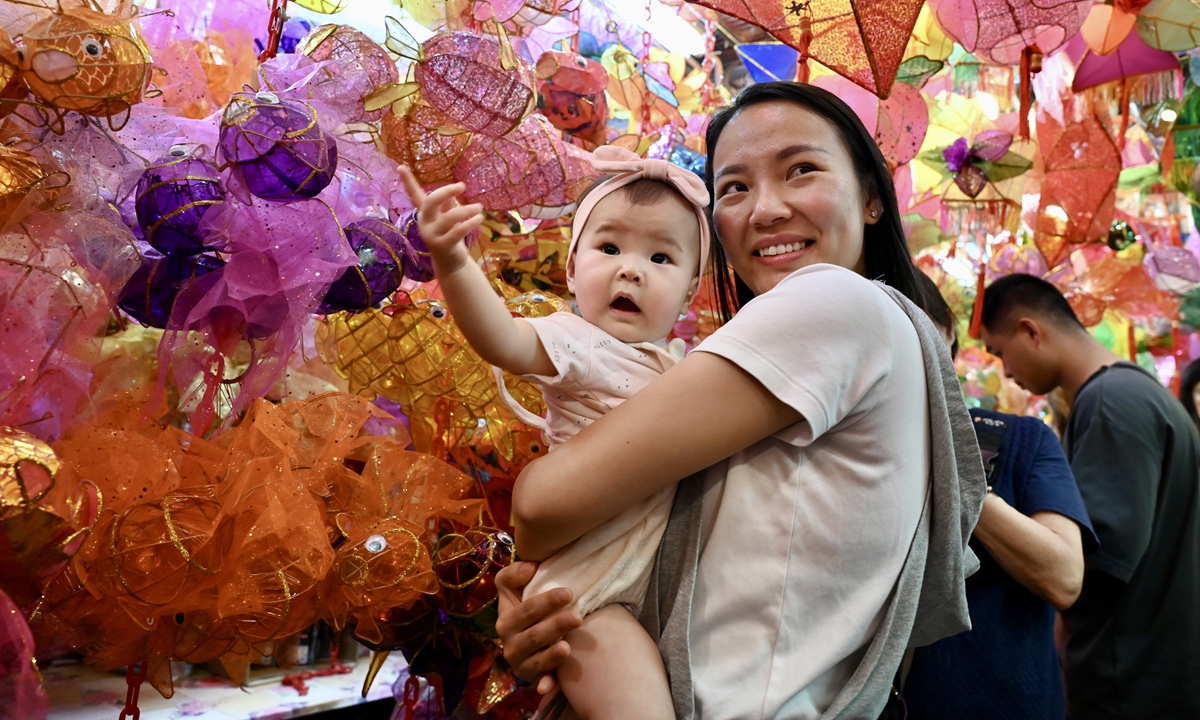 A mother holds her child in her arms while shopping for traditional lanterns at the Lantern Street in Yuen Long Bridge Market, Hong Kong Special Administrative Region, on September 20, 2023, ahead of the Mid-Autumn Festival. The festival, celebrated on the 15th day of the eighth month of the Chinese calendar, is usually marked by family reunions, a full moon viewing and the consumption of mooncakes. Photo: VCG