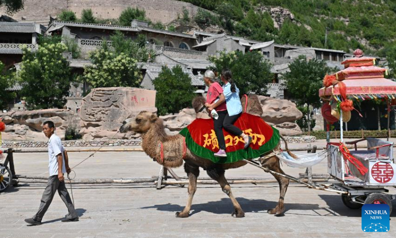 Villager Liu Jintu (L) leads his camel in the Qikou ancient town of Linxian County, north China's Shanxi Province, Aug. 2, 2023. Seeing the rapid development of tourism in the Qikou ancient town, Liu quit his job at construction sites. He bought a camel in 2016 and provided it to tourists for rides. Qikou, an ancient riverine town along the Yellow River, was an important trade ferry in history. However, with the development of land transportation, the Qikou ancient town declined in terms of trade volume, leaving many of its historical buildings in disrepair. In recent years, local authorities have carried out protection and restoration of historical buildings and ancient dwellings in the Qikou ancient town. At the same time, the integrated development of culture and tourism is also promoted. Today the ancient town has become a popular tourist attraction. More than 5,000 people out of a population of about 30,000 in the town are engaged in the tourism industry.（Photo：Xinhua）