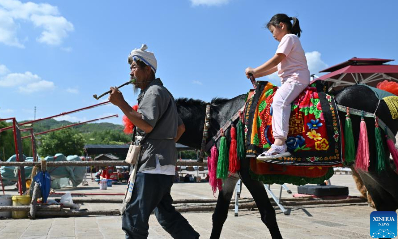 Villager Li Yonglin leads his donkey in the Qikou ancient town of Linxian County, north China's Shanxi Province, Aug. 2, 2023. Li would decorate his donkey and provide it to tourists for riding amid slack season of agricultural production. Qikou, an ancient riverine town along the Yellow River, was an important trade ferry in history. However, with the development of land transportation, the Qikou ancient town declined in terms of trade volume, leaving many of its historical buildings in disrepair. In recent years, local authorities have carried out protection and restoration of historical buildings and ancient dwellings in the Qikou ancient town. At the same time, the integrated development of culture and tourism is also promoted. Today the ancient town has become a popular tourist attraction. More than 5,000 people out of a population of about 30,000 in the town are engaged in the tourism industry. （Photo：Xinhua）