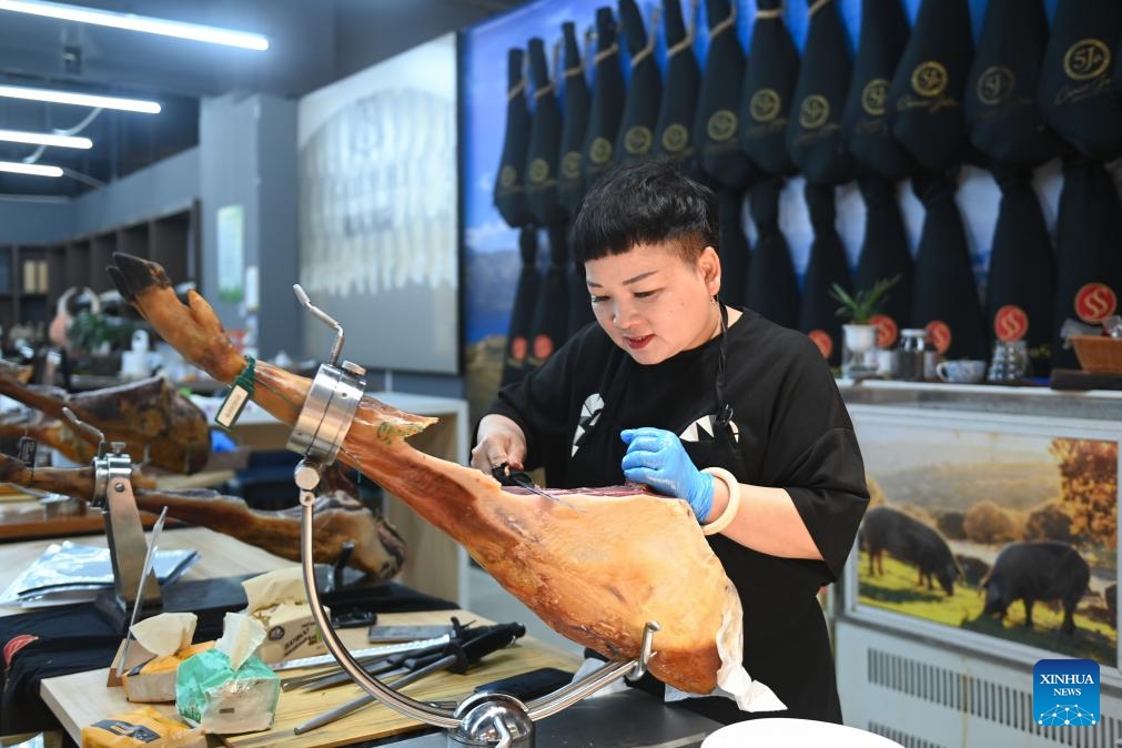 A shop owner of Spanish goods slices Iberian ham at the Yiwu International Trade Market in Yiwu, east China's Zhejiang Province, July 18, 2023. The train service from the Chinese small commodity hub of Yiwu to the European commodity center of Madrid was officially launched in November 2014, spanning eight countries in Eurasia with a total length of more than 13,000 kilometers.(Photo: Xinhua)