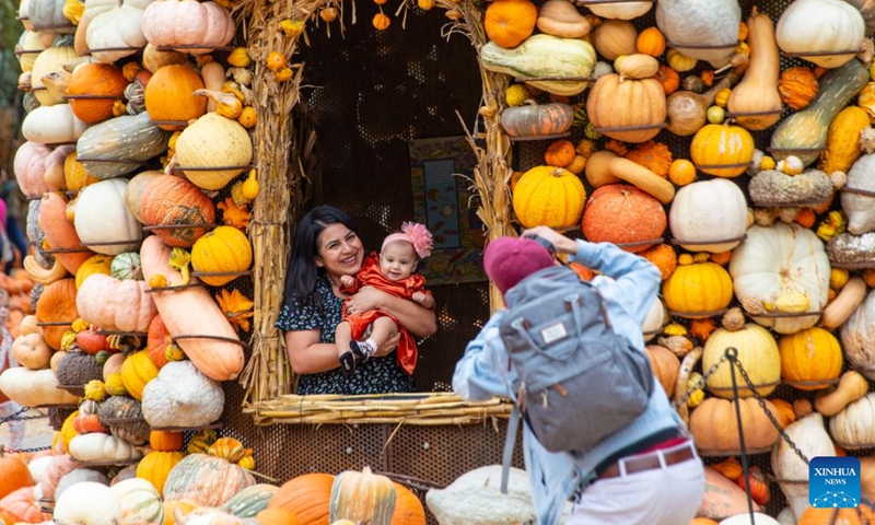 A woman holding a baby poses for a photo in Dallas Arboretum's Pumpkin Village, Texas, the United States, on Oct. 12, 2023. The nationally-acclaimed Pumpkin Village at Dallas Arboretum features pumpkin houses and creative displays fashioned from more than 100,000 pumpkins, gourds and squash. (Photo:Xinhua)