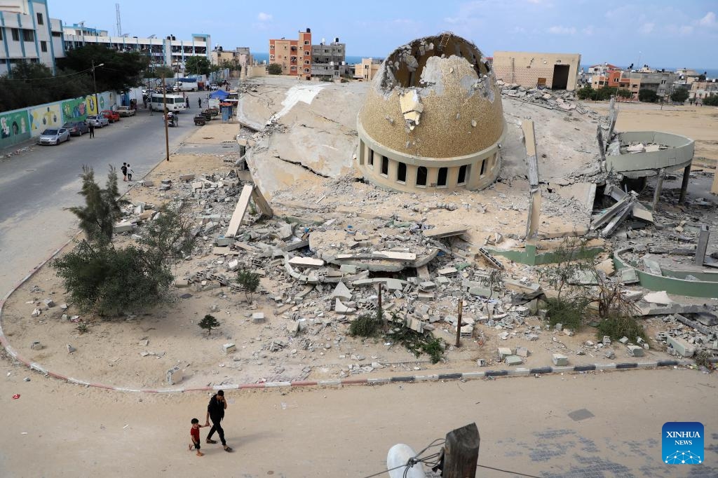 People walk past a building destroyed in Israeli airstrikes in the southern Gaza Strip city of Khan Younis, on Oct. 16, 2023. At least 2,750 Palestinians were killed by the Israeli army in Gaza, while in Israel, the death toll was at least 1,284 as of Sunday, according to official figures from the two sides.(Photo: Xinhua)