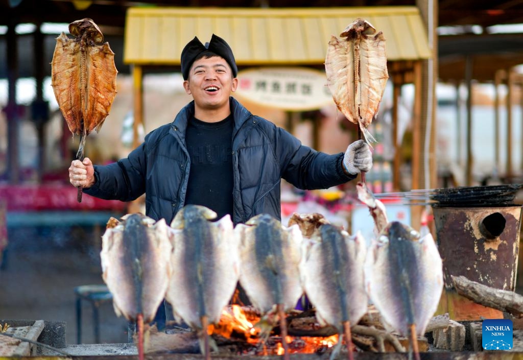 A vendor promotes grilled fish at a scenic spot in Yuli County, northwest China's Xinjiang Uygur Autonomous Region, Nov. 3, 2023. It is the best viewing period of the year for the desert poplar (populus euphratica) forest in the Tarim River Basin of Xinjiang. Approximately 15 million mu (1 million hectares) of desert poplar forest are distributed here, making it the largest desert poplar forest in the world.(Photo: Xinhua)