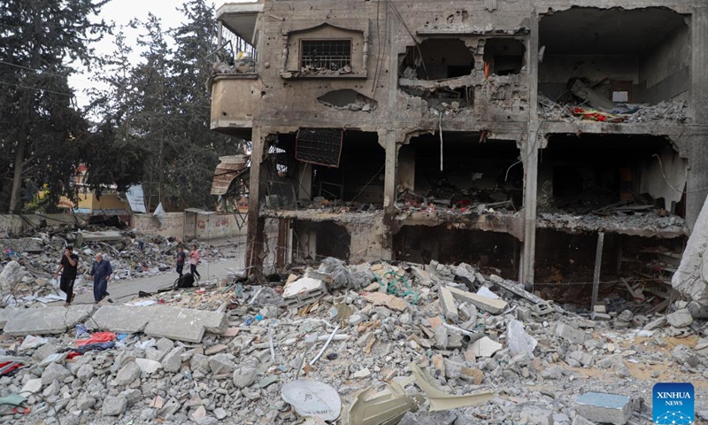 People walk past the rubble of buildings destroyed in Israeli airstrikes in the southern Gaza Strip city of Khan Younis on Nov. 12, 2023. The government media office in Gaza on Sunday announced that the casualties from Israeli attacks climbed to 11,180, including nearly 8,000 children and women, with more than 28,000 injuries.(Photo: Xinhua)