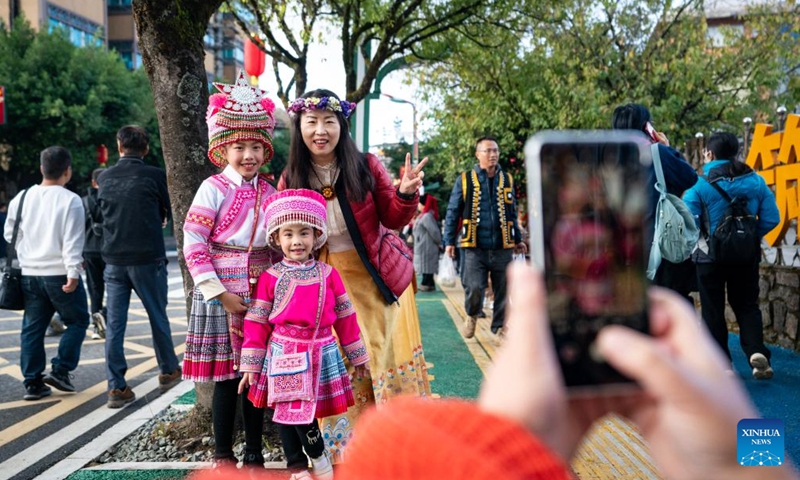 A tourist poses for a photo with local children during a cultural tourism festival in Luchun County of Honghe Hani and Yi Autonomous Prefecture, southwest China's Yunnan Province, Nov. 19, 2023. The long street banquet, a time-honoured tradition of Hani ethnic group in China, was held here during a cultural tourism festival on Sunday. (Photo: Xinhua)