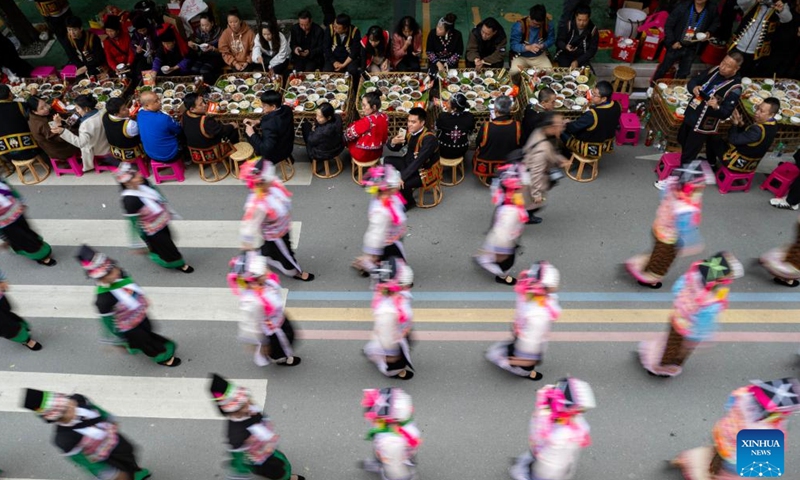 This aerial photo taken on Nov. 19, 2023 shows tourists and local residents taking part in the long street banquet as performers passing by during a cultural tourism festival in Luchun County of Honghe Hani and Yi Autonomous Prefecture, southwest China's Yunnan Province. The long street banquet, a time-honoured tradition of Hani ethnic group in China, was held here during a cultural tourism festival on Sunday. (Photo: Xinhua)