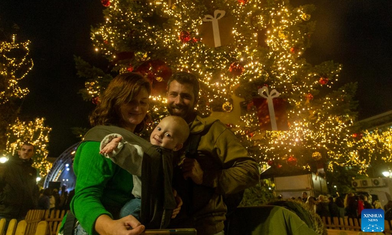 A family poses in front of an illuminated Christmas tree at Syntagma Square in Athens, Greece, on Nov. 23, 2023. The holiday season kicked off in Athens with a tree lighting ceremony on Thursday. (Photo: Xinhua)