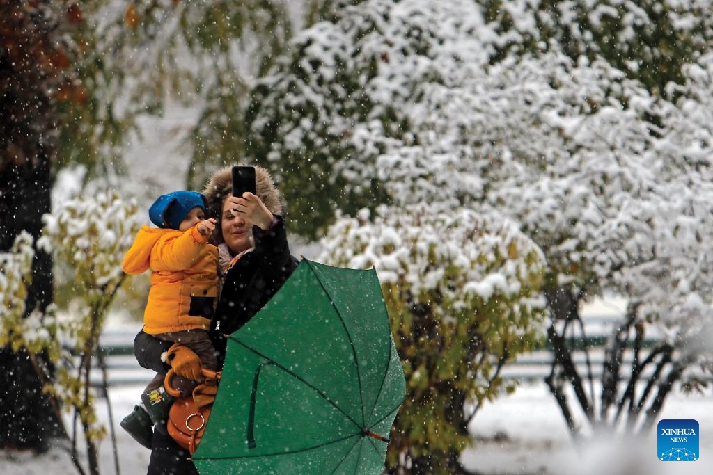 A woman holding a child takes a selfie in a park during a snowfall in Bucharest, Romania, on Dec. 7, 2023. Romania greeted the first snowfall of this year's winter on Thursday.(Photo: Xinhua)