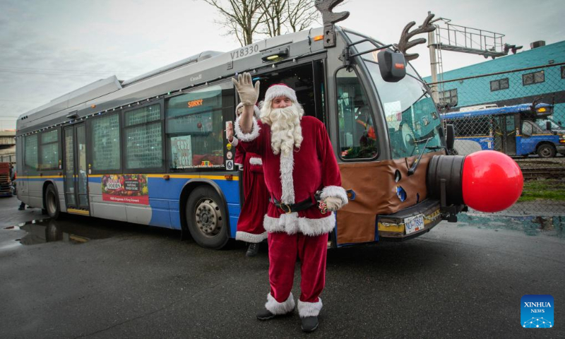 A staff member of bus company dressed as Santa Claus poses in front of a decorated bus during the Toys for Tots event in Vancouver, British Columbia, Canada, Dec. 15, 2023. (Photo by Liang Sen/Xinhua)