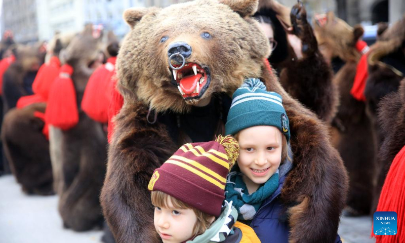 Children and a masked member of a traditional song and dance band pose for photos during the 