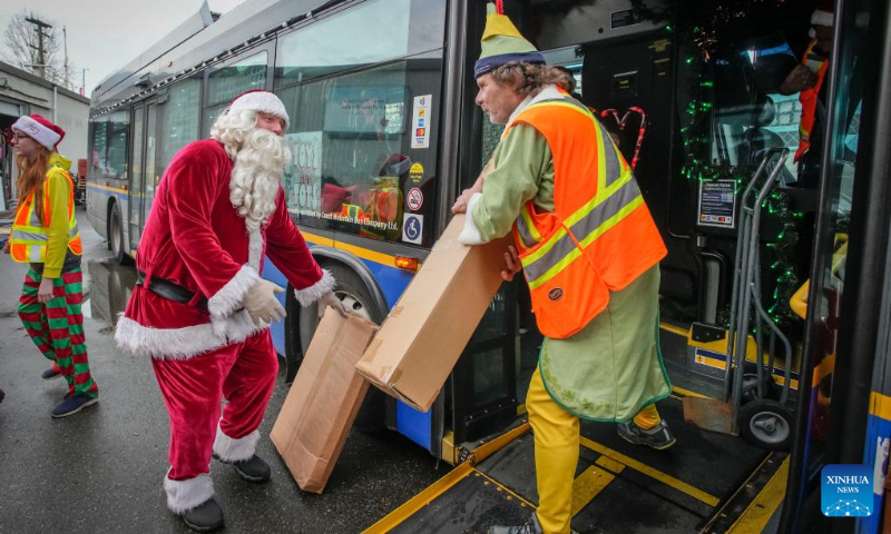 Staff members of bus company dressed in Christmas costumes unload toys from a bus during the Toys for Tots event in Vancouver, British Columbia, Canada, Dec. 15, 2023. (Photo by Liang Sen/Xinhua)