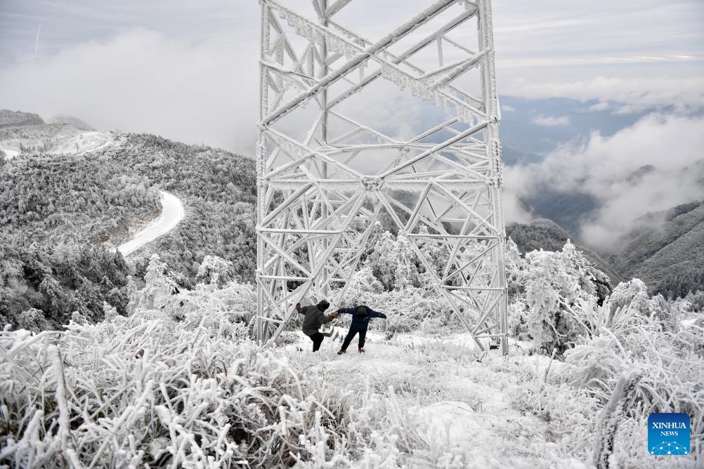 Power supply technicians Yin Bin (R) and Long Yujun return after checking the icing condition of a power transmission tower at an observation station on Xihuang Mountain on the border between Zhijiang Dong Autonomous County and Mayang Miao Autonomous County of Huaihua, central China's Hunan Province, Dec. 19, 2023. Due to the recent strong cold wave sweeping across Hunan Province, some power transmission lines crossing Xihuang Mountain experienced icing.（Photo: Xinhua)