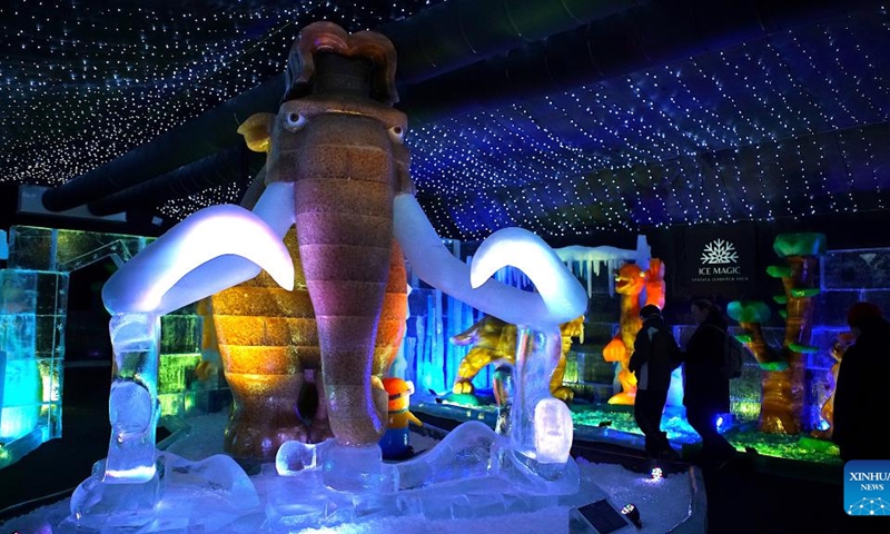 Visitors walk past a mammoth ice sculpture at the Ice Magic exhibition in Prague, the Czech Republic, on Dec. 19, 2023. Ice Magic, an ice exhibition displaying various characters of fairy tales and cartoons, is held here from Dec. 11, 2023 to April 2024.（Photo: Xinhua)