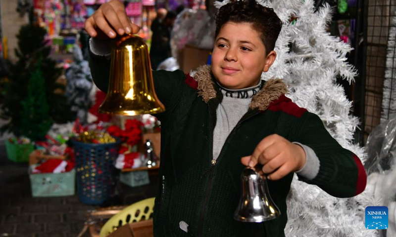 A boy holds bells at a market of Christmas decorations in Damascus, Syria, Dec. 23, 2023. (Photo by Ammar Safarjalani/Xinhua)