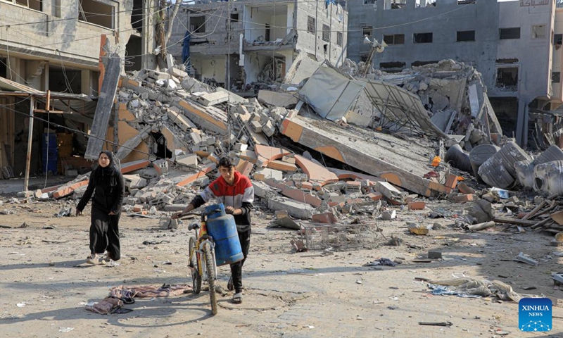 People walk past buildings destroyed in Israeli strikes in the southern Gaza Strip city of Khan Younis, on Jan. 4, 2024. Palestinian death toll from Israeli strikes on the Gaza Strip rose to 22,438 since the Israel-Hamas conflict broke out on Oct. 7, 2023, said the Gaza-based Health Ministry on Thursday.(Photo: Xinhua)