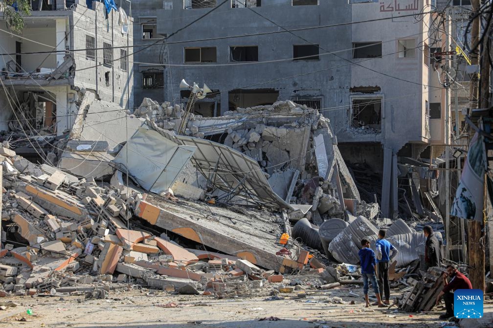 People are seen in front of buildings destroyed in Israeli strikes in the southern Gaza Strip city of Khan Younis, on Jan. 4, 2024. Palestinian death toll from Israeli strikes on the Gaza Strip rose to 22,438 since the Israel-Hamas conflict broke out on Oct. 7, 2023, said the Gaza-based Health Ministry on Thursday.(Photo: Xinhua)