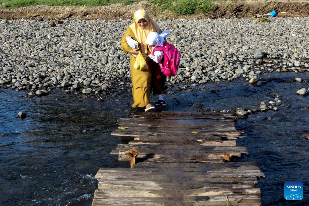 A woman holding a student walks on a temporary wooden bridge on the way to school at a village in West Sumatra, Indonesia, Jan. 8, 2024(Photo: Xinhua)