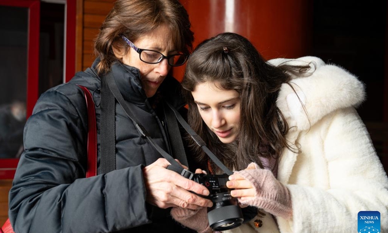 Carly Beth (R) checks the photos her mother took for her at the Confucian Temple in Beijing, capital of China, Jan. 17, 2024.(Xinhua/Hu Zhixuan)