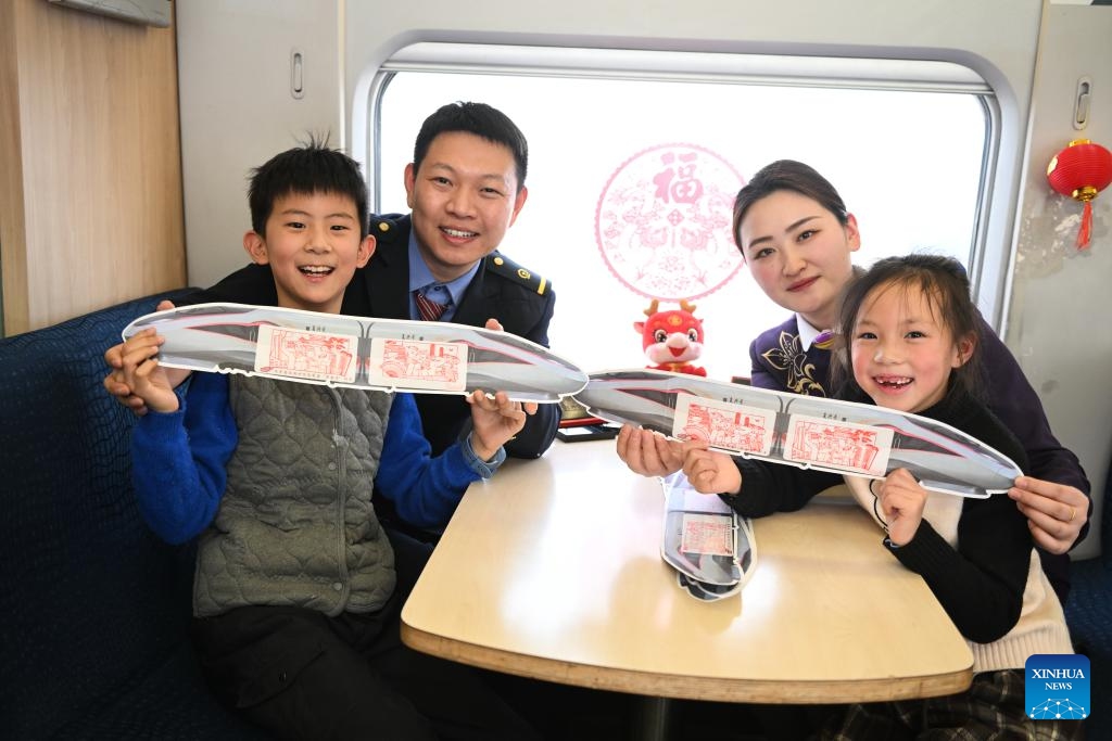 Staff members and young passengers show souvenirs onboard G7575 bullet train, Jan. 29, 2024. A series of traditional cultural activities, such as opera performance and paper cutting show, were held on the bullet train on Monday. China officially ushered in its largest annual population migration on Jan. 26. The 40-day travel surge, also known as chunyun, will see hundreds of millions of people return home and reunite with their friends and families.(Photo: Xinhua)