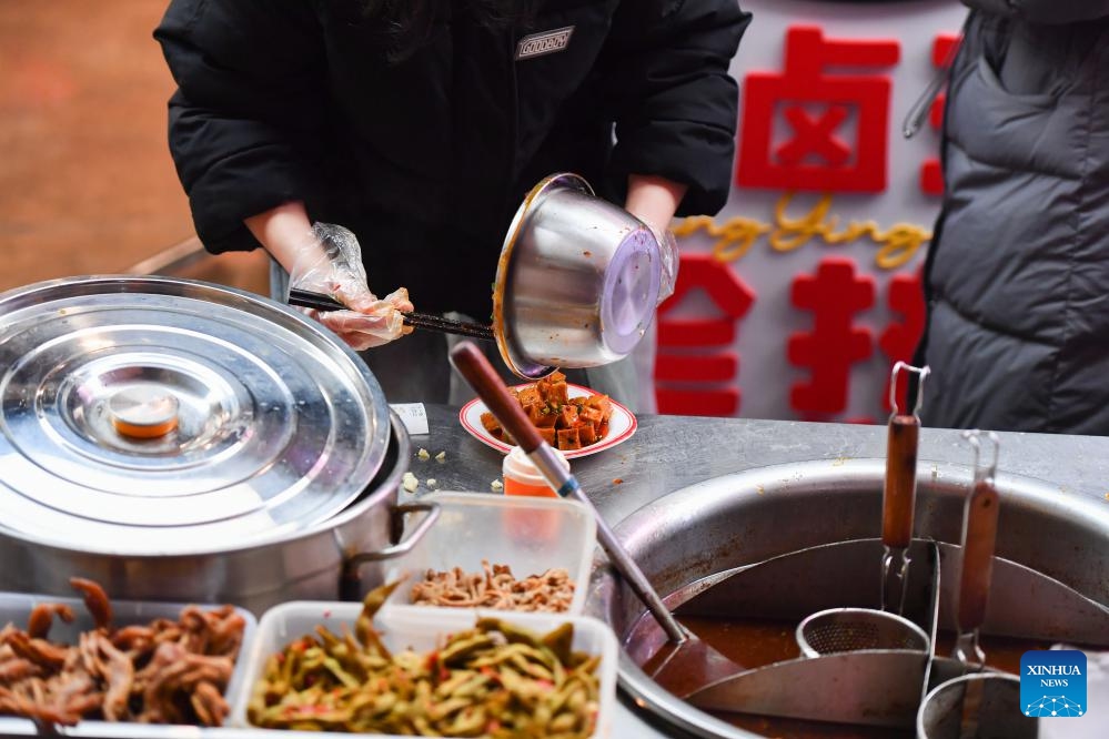 A staff member prepares marinated food at a stall in a night market selling street food in Changsha, central China's Hunan Province, Feb. 4, 2024. To attract more visitors, stalls in this night market are making innovations such as developing new products and promoting via social media.(Photo: Xinhua)