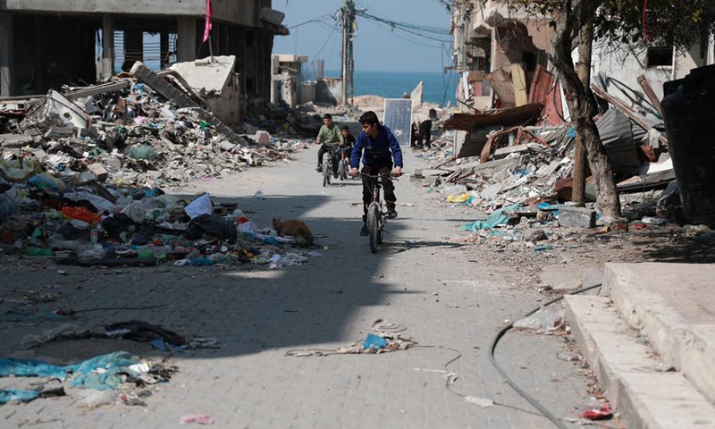 Children ride past destroyed buildings in Gaza City, Feb. 26, 2024.(Photo: Xinhua)