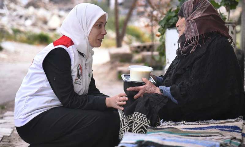 A volunteer from the team Youth Impression of Syria distributes free meal to a woman on the outskirts of Damascus, Syria, March 22, 2024. (Photo by Ammar Safarjalani/Xinhua)