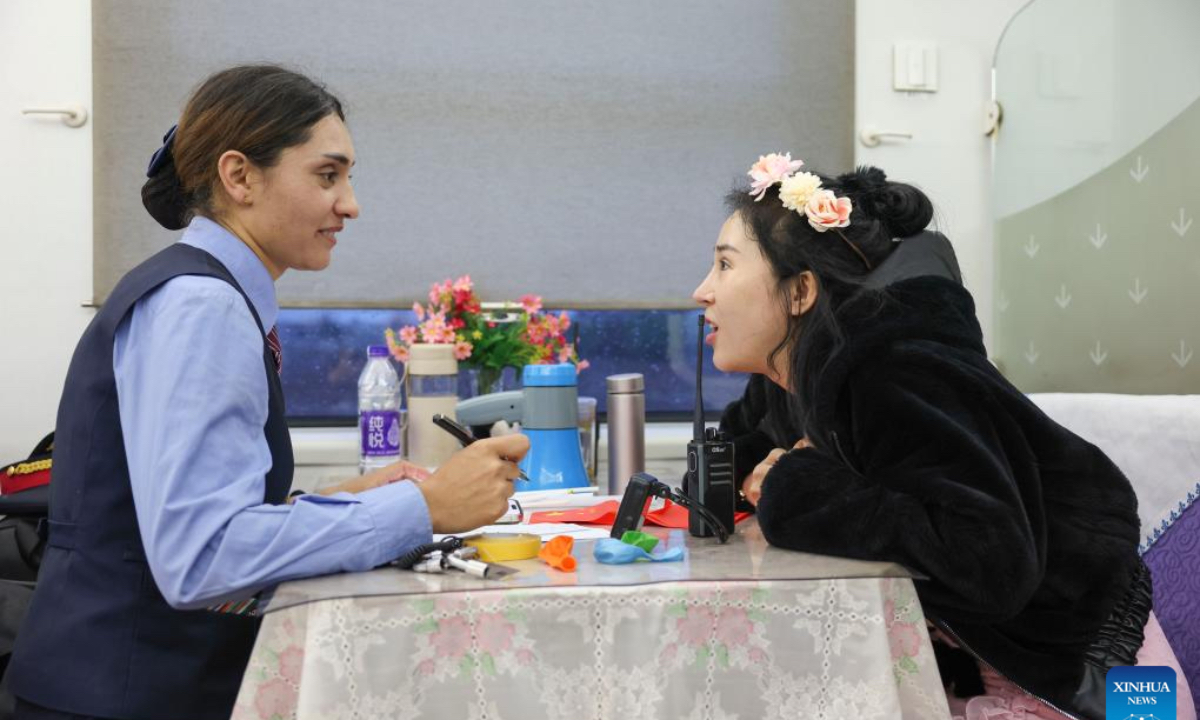 Airkir Duliki (L) tells a passenger about tourism on the Pamir Plateau on a train from Kashgar to Chengdu in China, April 19, 2024. Airkir Duliki, the 27-year-old ethnic Tajik train conductor, was born and raised amidst the snow-capped mountains and grasslands in a village of Taxkorgan Tajik Autonomous County on the Pamir Plateau, where railways were not common for residents in the past. Airkir's initial experience with train travel occurred when she journeyed to Urumqi for university in Xinjiang. Accompanied by her father, she traversed over 300 kilometers of mountainous terrain from their village to reach the nearest Kashgar train station. Inspired by the first train journey, Airkir pursued a career in the railway sector after graduating from university in 2019. Since then, she has served as a train attendant on routes, linking Kashgar of northwest China's Xinjiang Uygur Autonomous Region and Chengdu of southwest China's Sichuan Province. Throughout her four-years as an attendant, she has consistently demonstrated proficiency in her duties. In 2023, she successfully completed a series of assessments and transitioned into the role of conductor. (Photo: Xinhua)