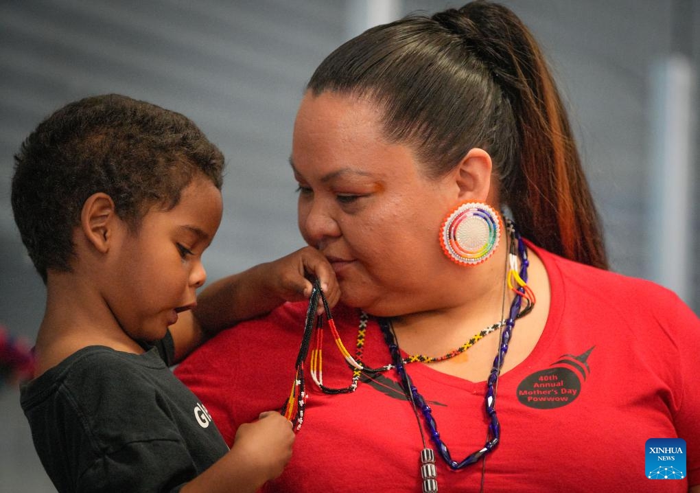 A woman holds her child during the Mother's Day Traditional Powwow in Vancouver, British Columbia, Canada, on May 12, 2024. Hundreds of indigenous people from various tribes across Canada gathered on Sunday to celebrate Mother's Day with a powwow, a traditional social gathering featuring music and dance.(Photo: Xinhua)