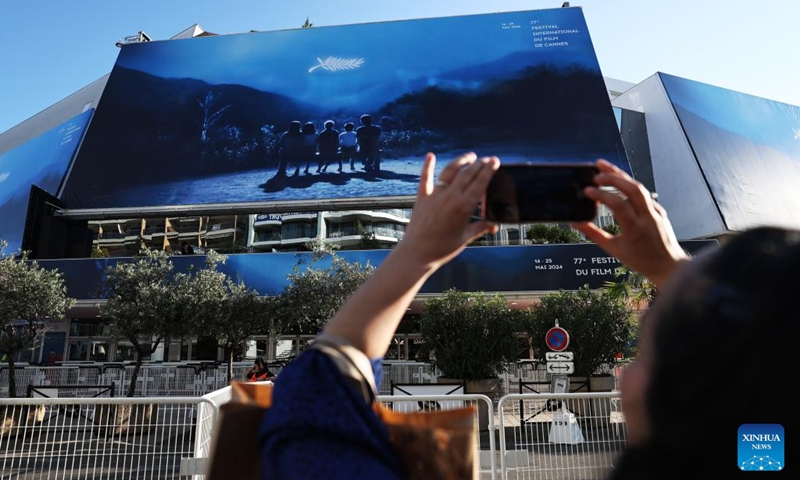 A woman takes photos of a huge poster of the 77th edition of the Cannes Film Festival outside the Palais du Festival in Cannes, southern France, May 13, 2024. This year's festival runs from May 14 to 25.(Photo: Xinhua)