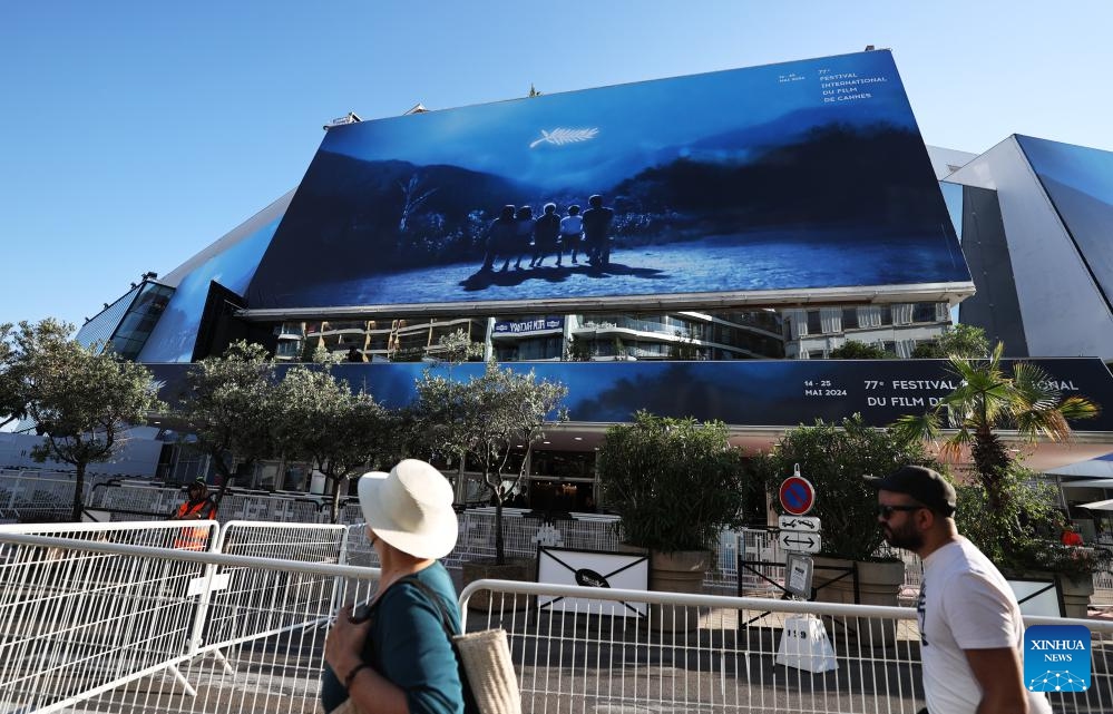 People walk past a huge poster of the 77th edition of the Cannes Film Festival outside the Palais du Festival in Cannes, southern France, May 13, 2024. This year's festival runs from May 14 to 25.(Photo: Xinhua)