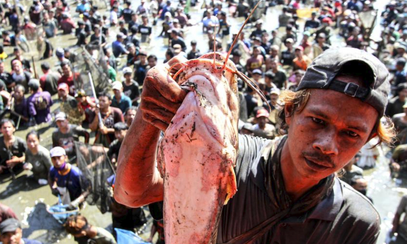 A man presents a catfish he caught during Festival Memet Ikan, or fish catching festival, at Gemblegan village in Klaten regency, Central Java, Indonesia, July 21, 2024. (Photo by Bram Selo/Xinhua)